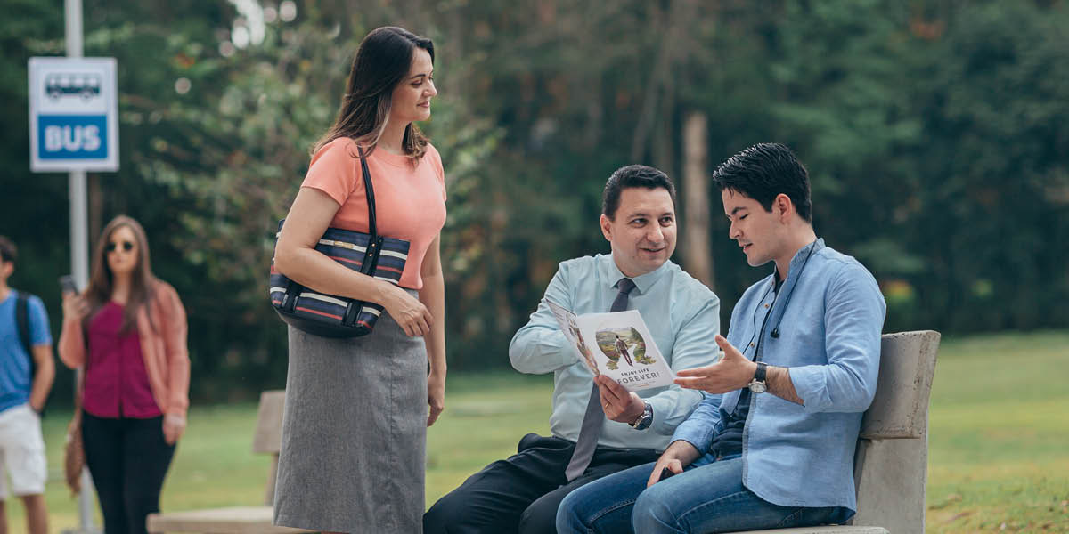 A couple using the “Enjoy Life Forever!” brochure to talk with a man at a bus stop.