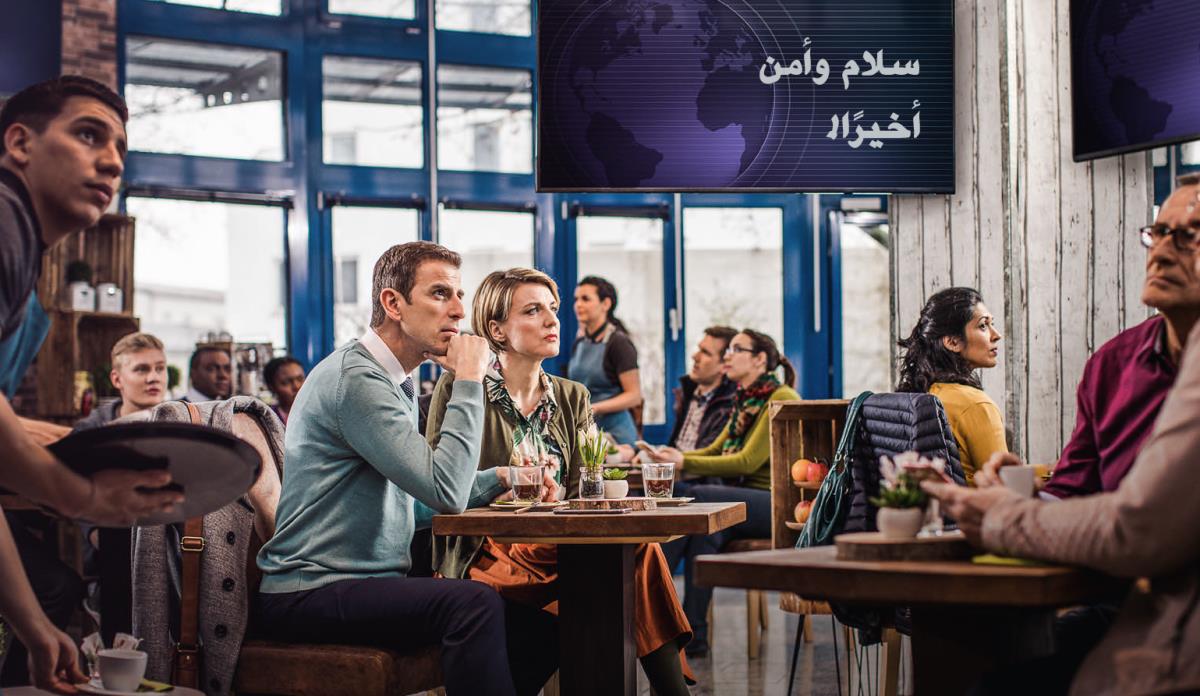 زبائن في مقهى يسمعون باهتمام «خبرا عاجلا» على التلفزيون عن اعلان ‹السلام والامن›،‏ لكن زوجين من الشهود لا ينخدعان به