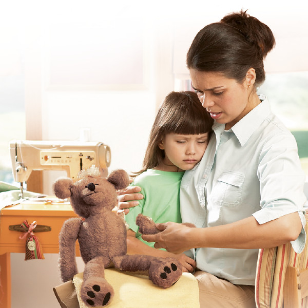 A mother consoles her daughter who is upset because an arm has come off her teddy bear