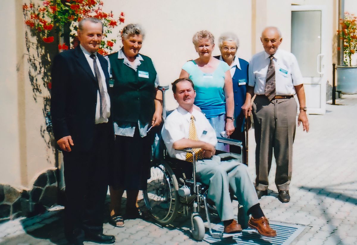 Ibolya and István, who is sitting in a wheelchair, posing for a photo with a group of friends.