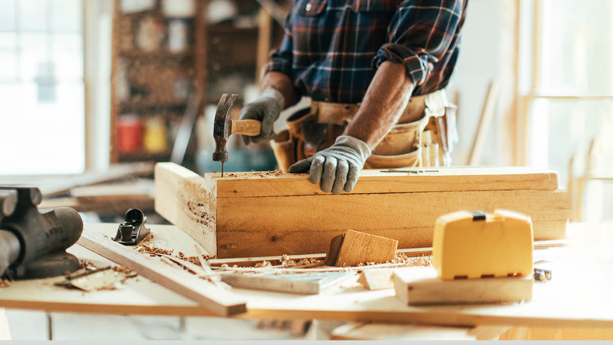 একজন কাঠমিস্ত্রি কাঠে পেরেক ঠুকছেন।