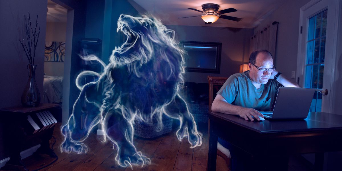 Un hermano usando una computadora por la noche y, junto a él, un león rugiente, que representa a Satanás