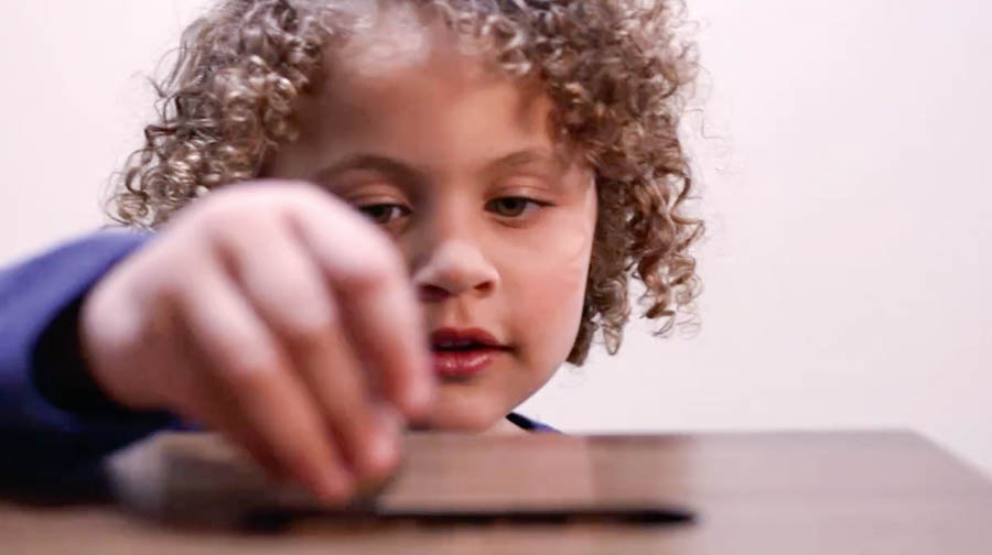 Una imagen del video Llenemos nuestra mano con una dádiva para Jehová: Una niña echando unas monedas en la caja de contribuciones del Salón del Reino.