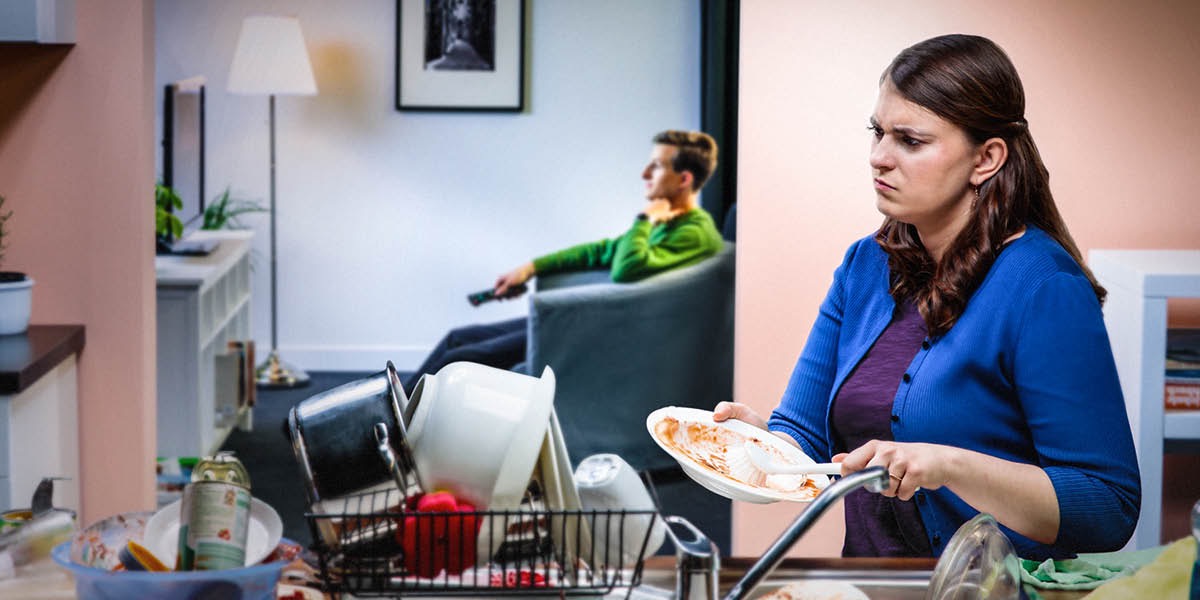 Una dona s’enfada amb el seu home perquè està mirant la tele mentres ella està escurant els plats