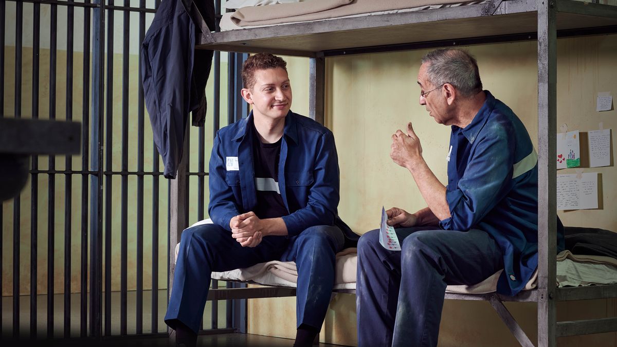 Dos germans conversant en una cel·la assentats en una llitera. Darrere d’ells hi han targetes, cartes i dibuixets penjats en la paret.