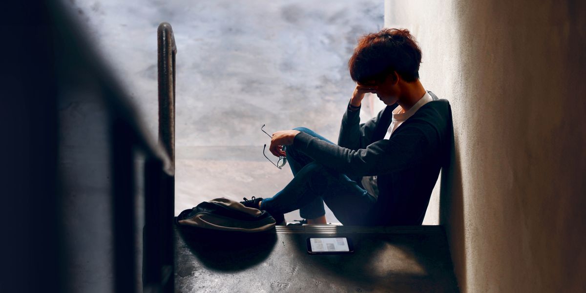 在昏暗的楼梯间，一个青少年孤独地坐在地上，用一只手撑着头。