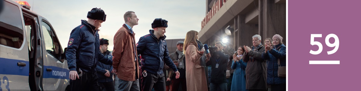 59. lekce. Dva policisté vedou bratra v poutech před přihlížejícími novináři a svědky Jehovovými