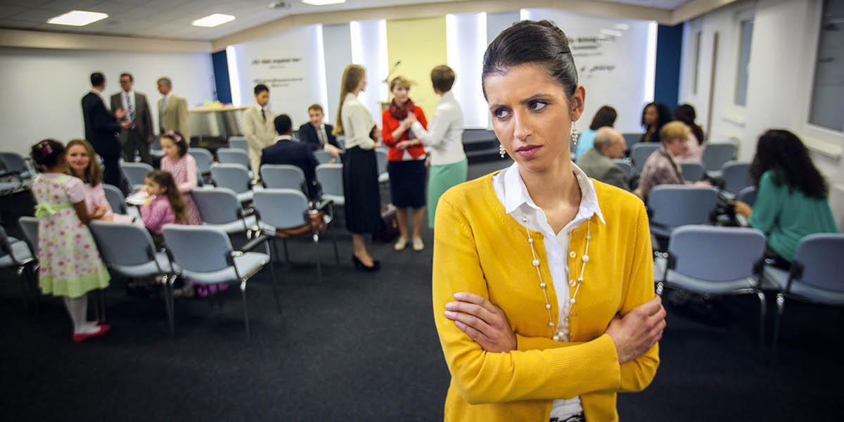 Nespokojená sestra stojí se založenýma rukama v sále Království stranou od ostatních