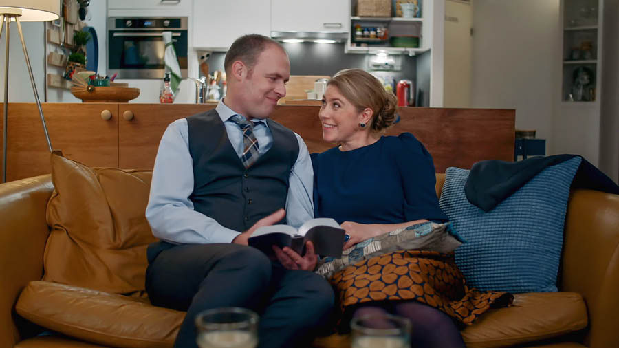 Scéna z videa „Projevuj neselhávající lásku v rodině“. Manželé se vrátili domů ze shromáždění a teď si spolu povídají o verši z Bible