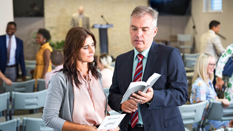 Starší ukazuje v Bibli verš sestře, která drží v ruce pozvánku na svatbu