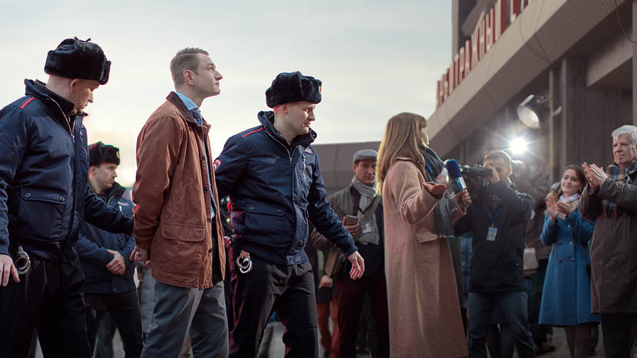 Policisté odvádějí zajatého bratra do vazby, sledují to reportéři a další bratři