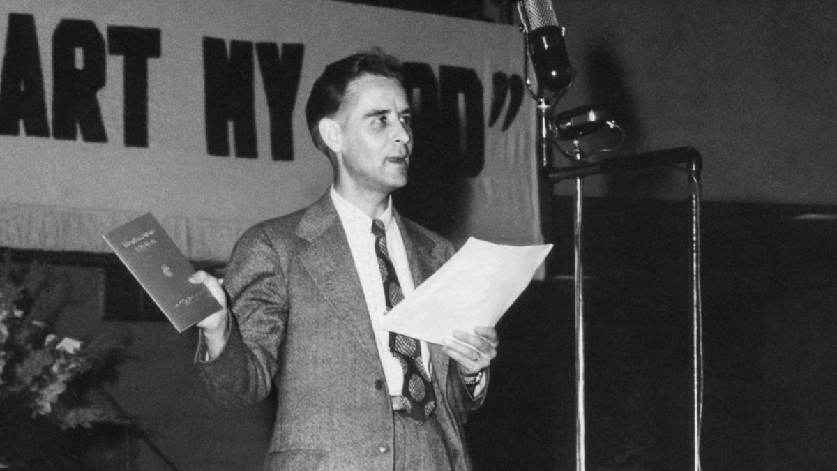 Scéna z videa „Naše živá historie: Zpěv je nádherný dar, 2. část“. Bratr F. W. Franz oznamuje vydání „Zpěvníku služby království“.