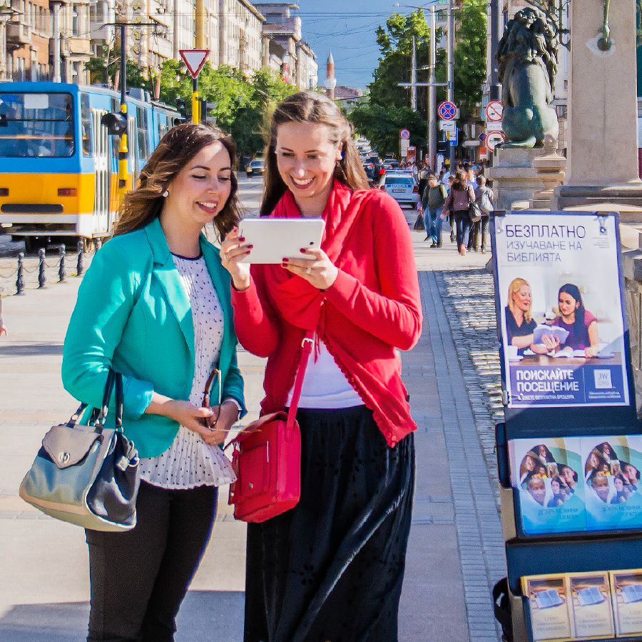 Sestra u stojanu s publikacemi mluví o Bibli s nějakou ženou