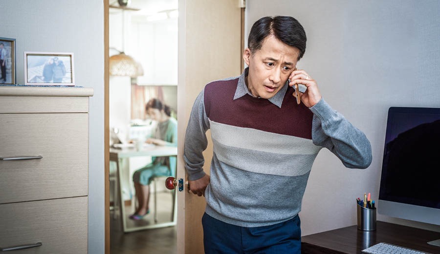 Starší mluví do telefonu a zavírá za sebou dveře od místnosti, ve které si studuje jeho manželka