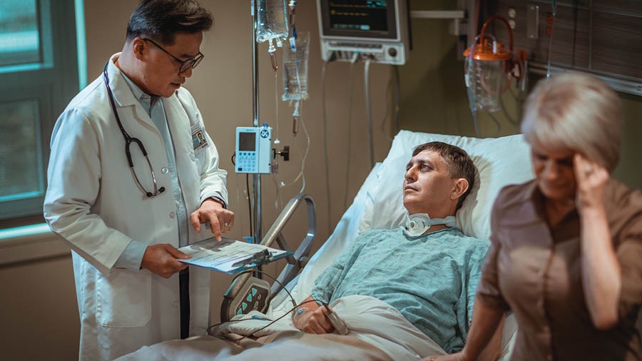 El hombre de la imagen anterior en la cama de un hospital. Su esposa se voltea mientras el doctor les da malas noticias sobre la salud de su esposo