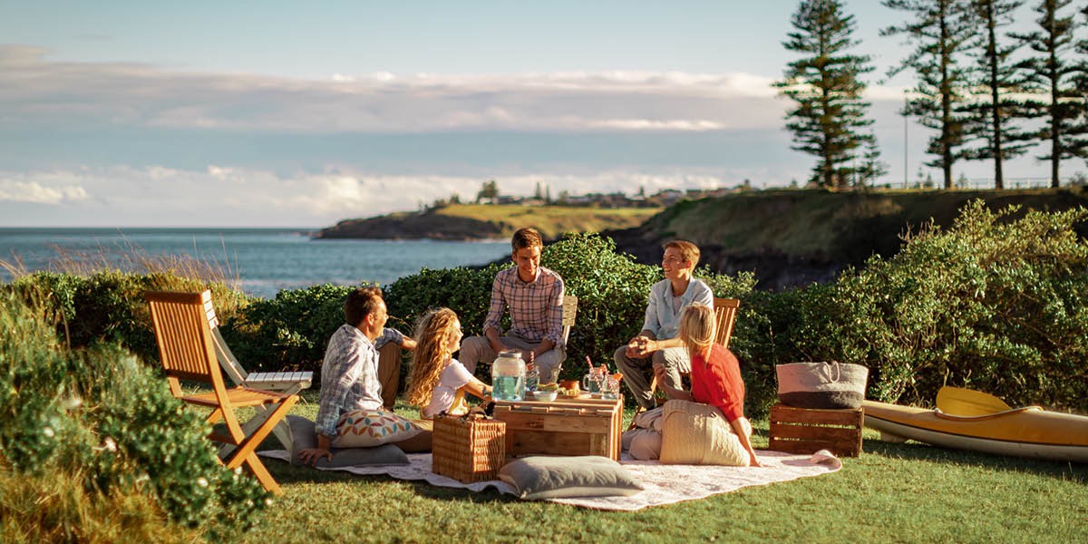 Una familia haciendo un pícnic junto al mar. Están tranquilos y se ríen.
