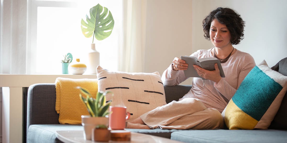 Una mujer sentada cómodamente en su sofá leyendo la Biblia