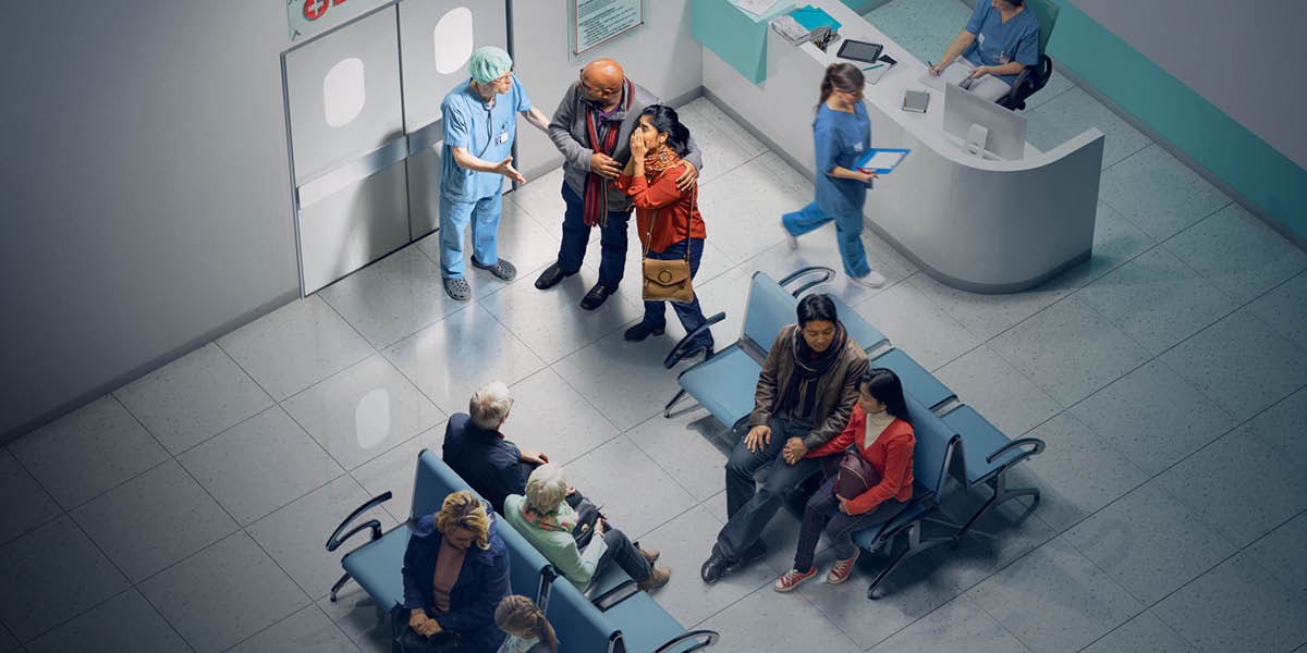 En la sala de espera de un hospital, un doctor le da malas noticias a un matrimonio que está cerca de una puerta. Otras personas esperan a que se les atienda.