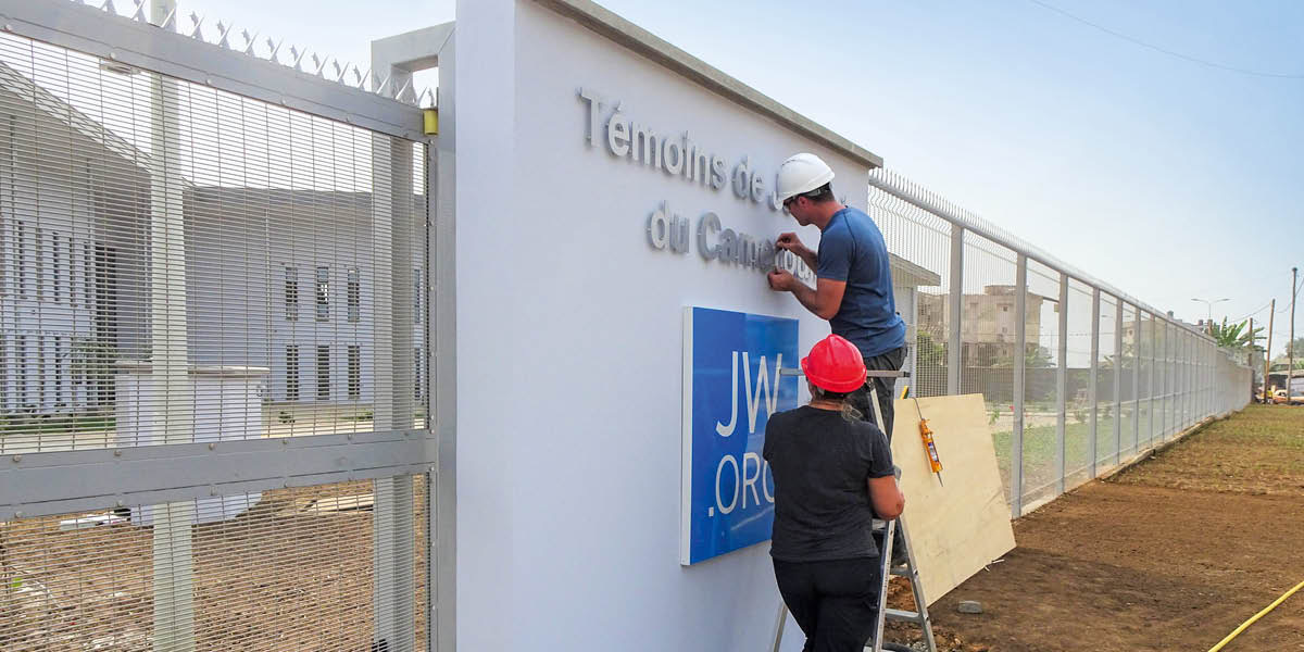 Voluntarios de construcción colocando el nuevo letrero en la entrada de la sucursal de Camerún.
