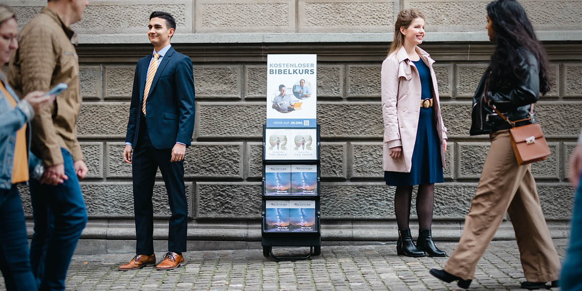 Un matrimonio sonriente junto a un exhibidor de publicaciones que anuncia nuestras clases gratuitas de la Biblia.