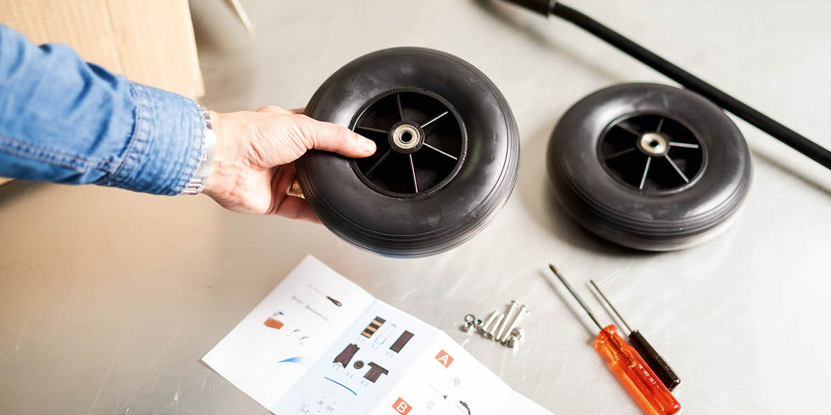 Instrucciones, herramientas y piezas de repuesto, como ruedas, una varilla, tuercas y tornillos, para reparar un carrito.