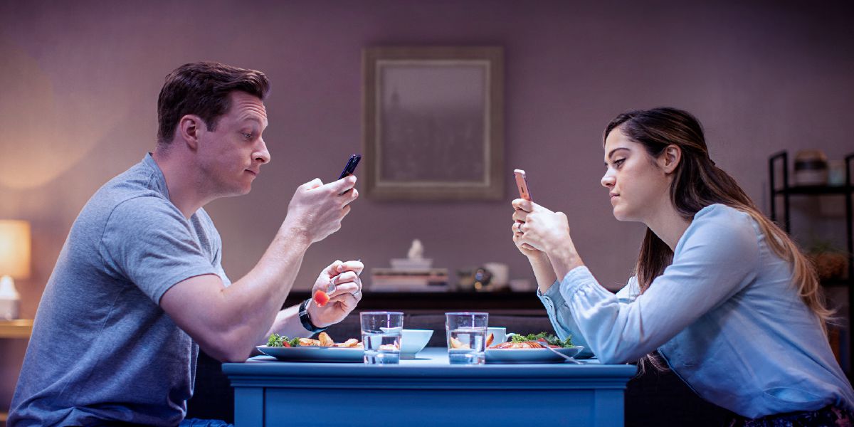 Un matrimonio está cenando mientras cada uno mira su teléfono.
