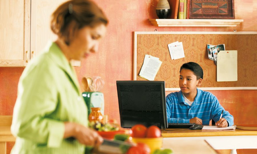 Un niño está en la cocina usando Internet mientras su madre prepara la comida
