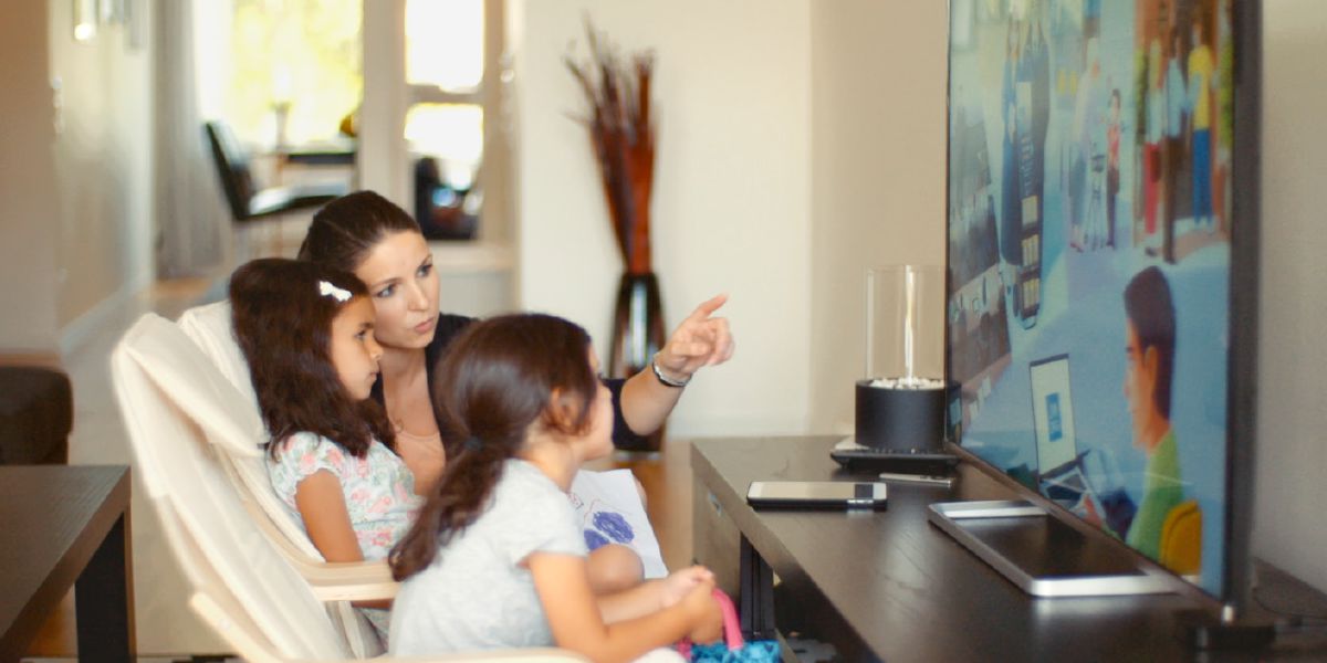 Talita mirando un video en jw.org con su madre y su hermana. Su madre le describe lo que se ve
