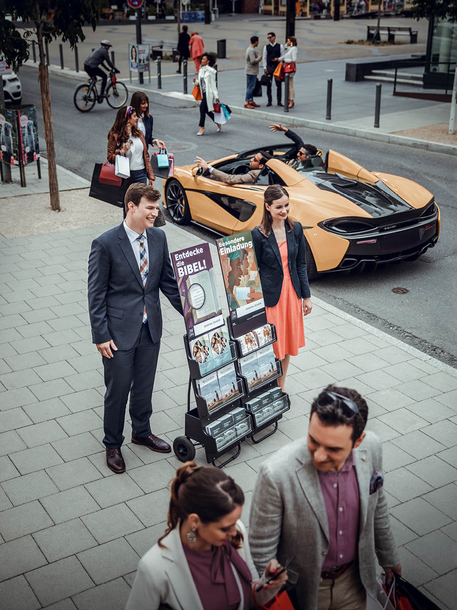 Un matrimonio joven en la predicación pública en una calle con gente comprando y con autos caros.