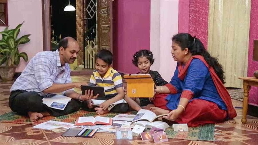 Una imagen del video Edifiquemos una casa que aguante. Protejamos a nuestros hijos de “lo que es malo”. Unos padres estudian con sus dos hijos el libro Aprendamos del Gran Maestro y otras publicaciones.