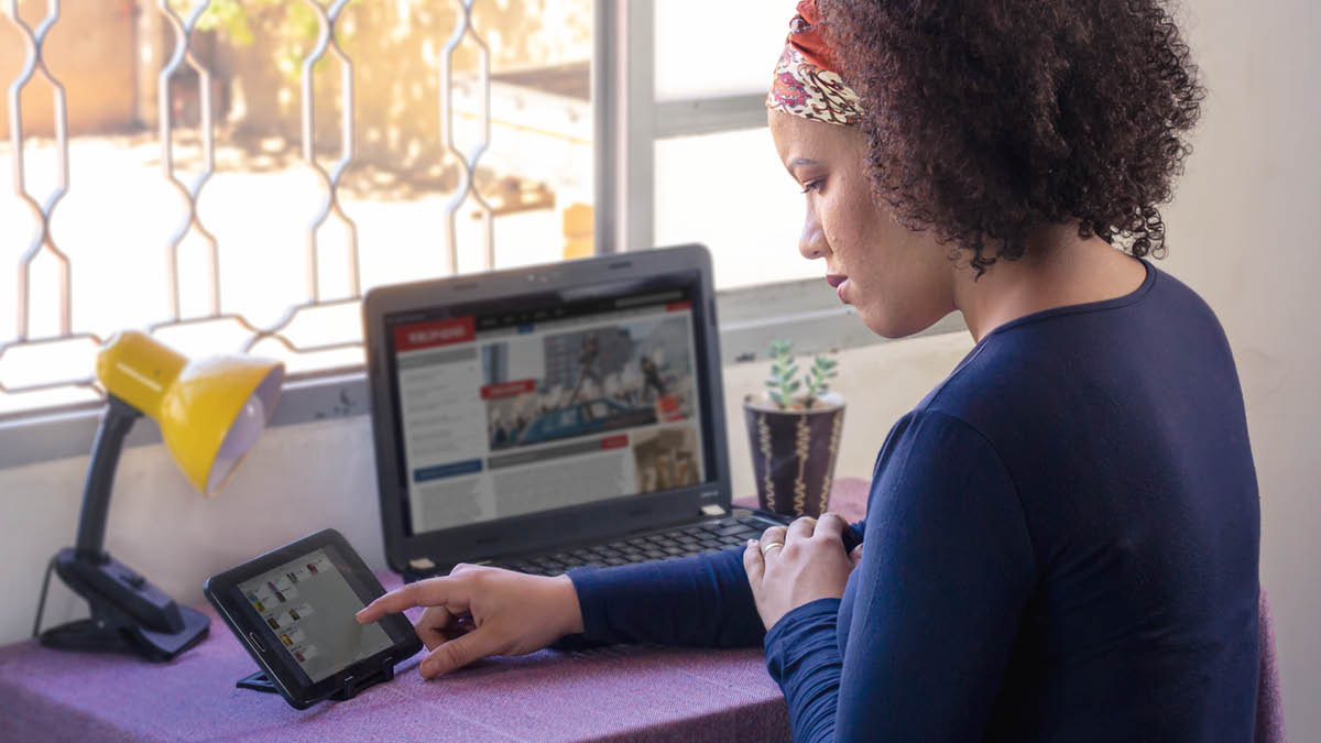 Una hermana se está preparando para predicar. Tiene un tratado en la mano y está mirando las noticias en su computadora.