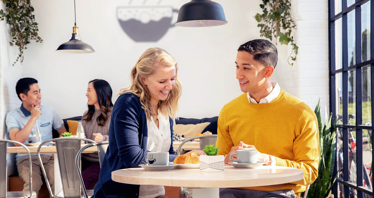 En una cafetería, una pareja de novios está hablando y se ríen.