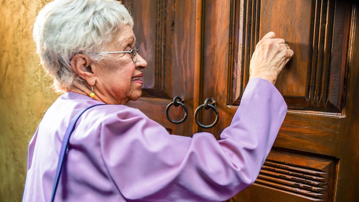 Una hermana mayor toca una puerta mientras predica de casa en casa.