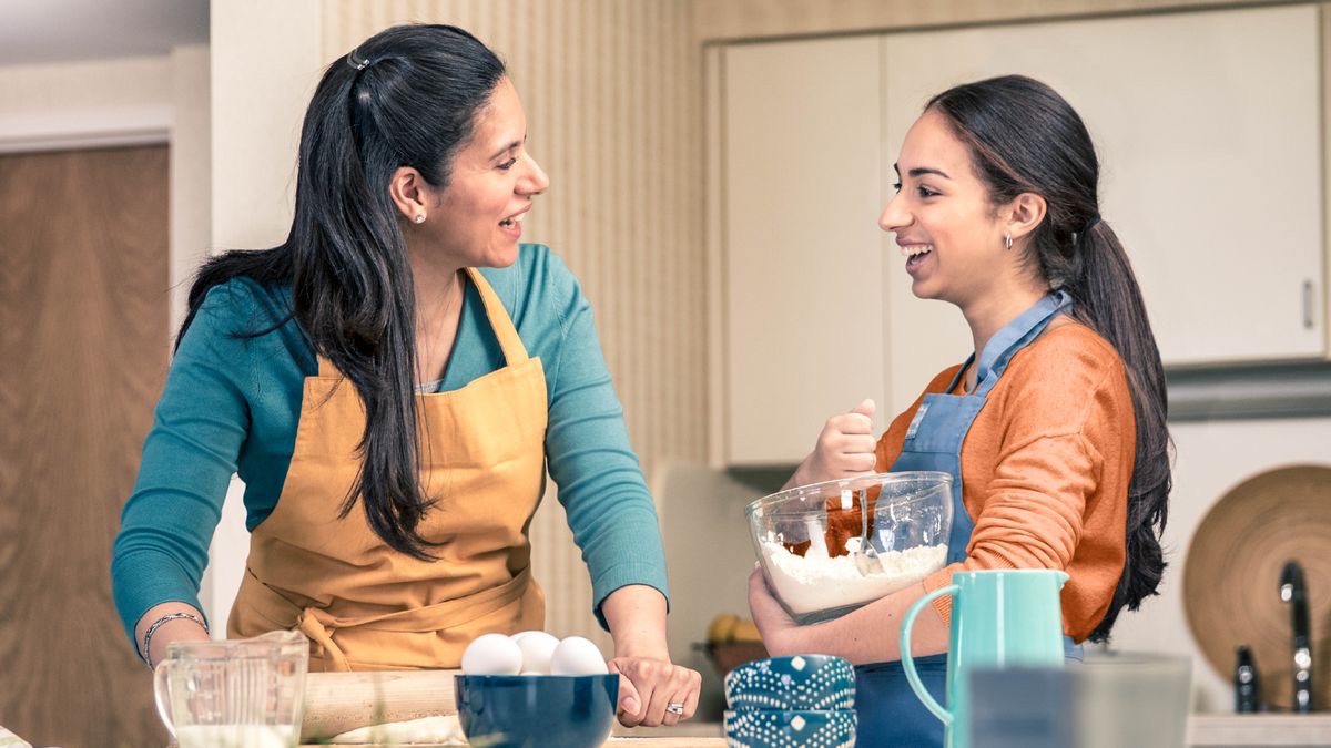 Una mamá y su hija hablan alegremente mientras preparan la comida.
