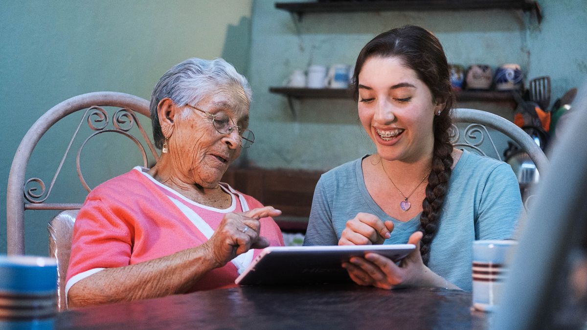 Una hermana joven le enseña a una hermana mayor a usar su tablet.