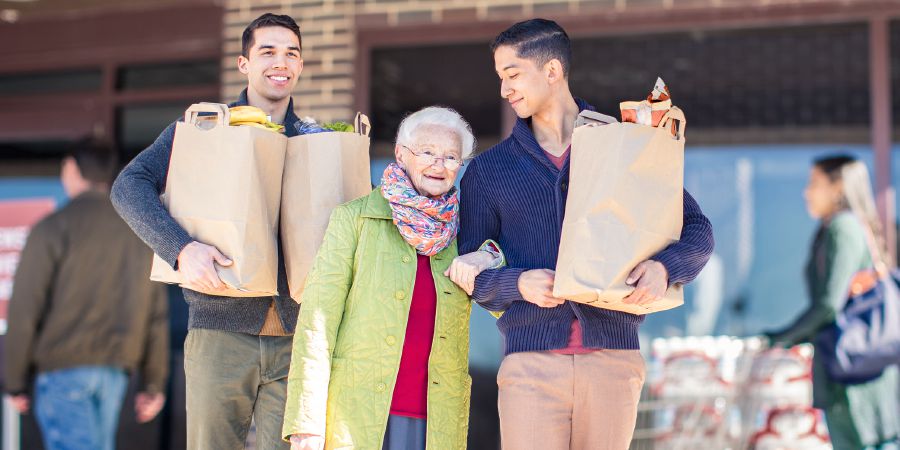 Dos hermanos jóvenes ayudan a una hermana mayor con las bolsas del supermercado