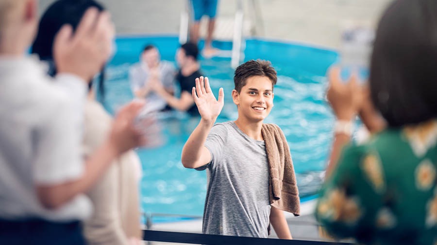 Un joven saluda a su familia y a sus amigos antes de entrar a la piscina para bautizarse