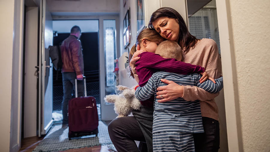 Un padre se va de su casa con una maleta. La madre abraza a sus dos hijos, que están llorando.