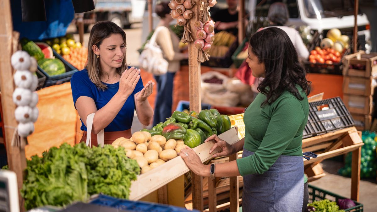 La misma hermana está en el mercado dándole una tarjeta de contacto de jw.org a una vendedora.