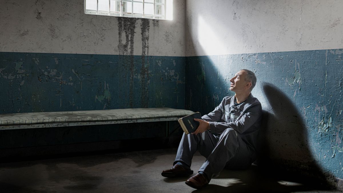 Un hermano que está encarcelado tiene una Biblia en las manos y mira por la ventana.