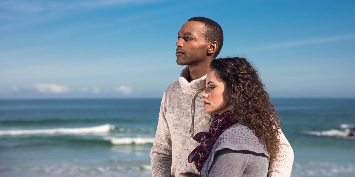 Un matrimonio que ha perdido a un ser querido mirando al horizonte en la playa mientras se abrazan