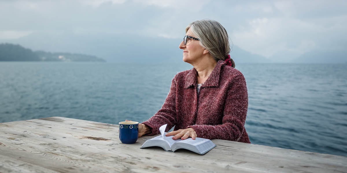 Una mujer sentada mirando al horizonte con una Biblia abierta sobre la mesa
