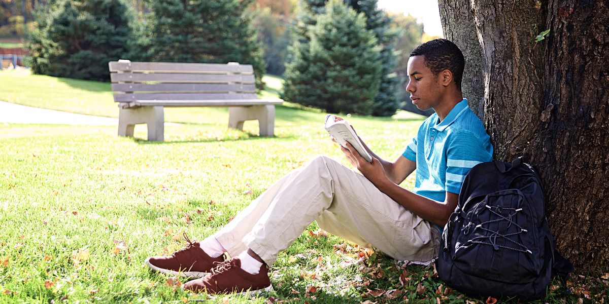 Un joven sentado bajo un árbol leyendo la Biblia