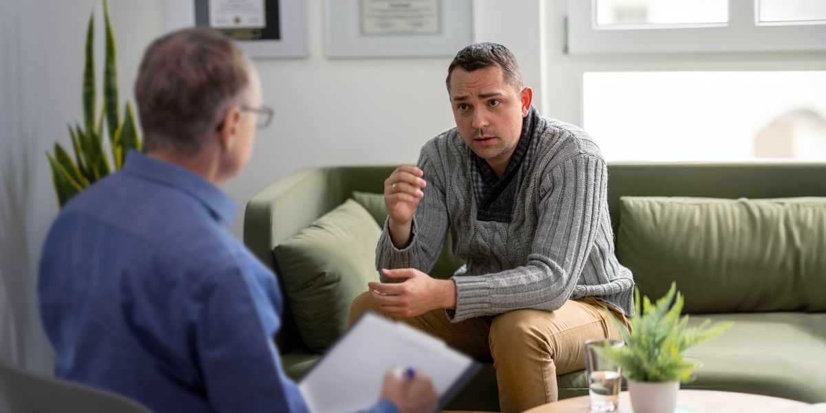 El esposo sentado en un sofá hablando con un profesional de la salud.