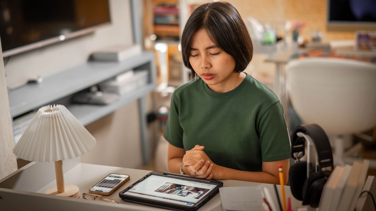 En ung søster sidder ved sit skrivebord og beder en bøn. På hendes tablet kan man se en artikel fra jw.org der handler om brødre og søstre som sidder i fængsel på grund af deres tro.