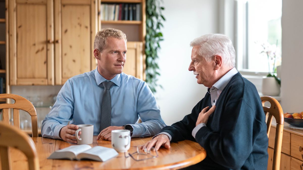 En ung ældste besøger en ældre bror i hans hjem og lytter opmærksomt til ham.