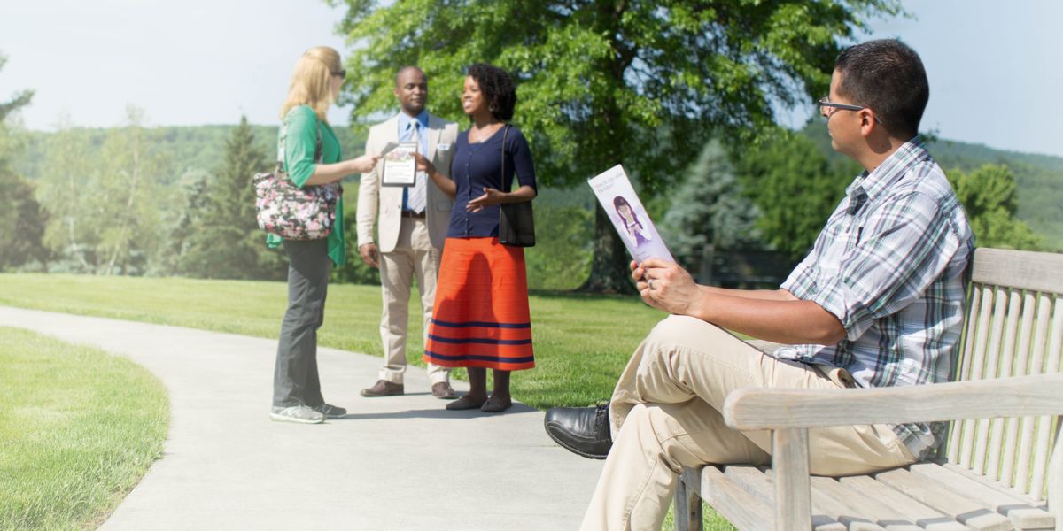 Ein Mann mit einem Faltblatt in der Hand beobachtet, wie Zeugen Jehovas mit einer Frau sprechen.