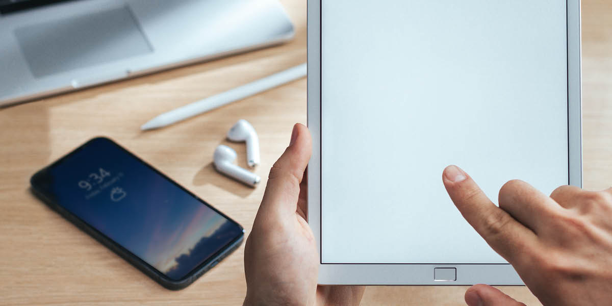 Una persona está usando una tablet y tiene otros dispositivos electrónicos cerca.