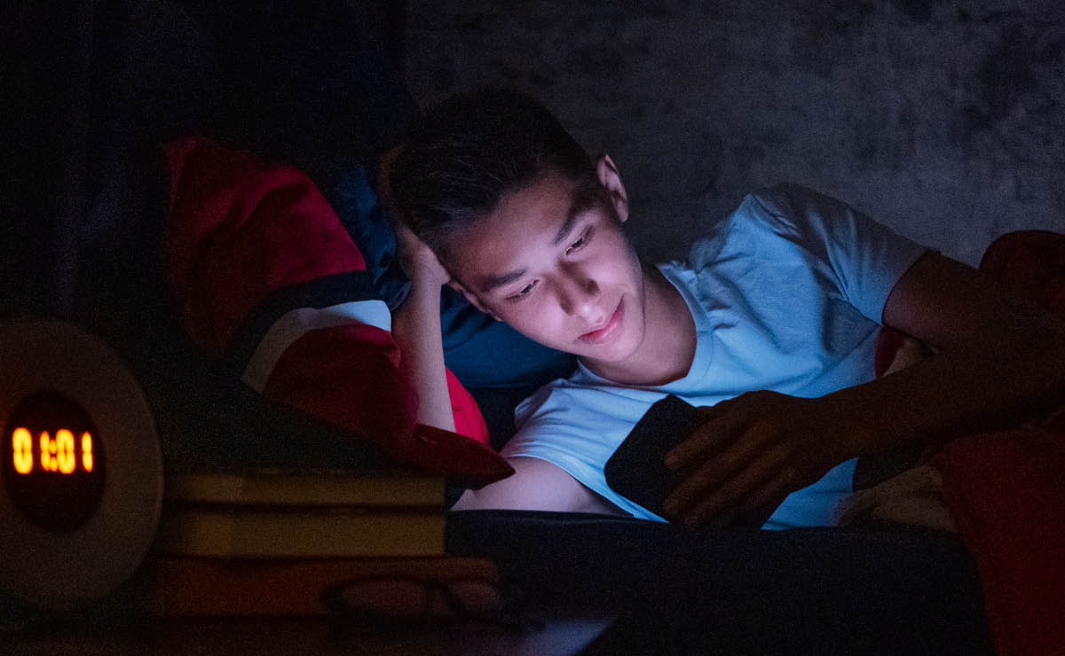 Es más de la una de la mañana y un adolescente sigue pegado a su celular mientras está acostado en la cama.