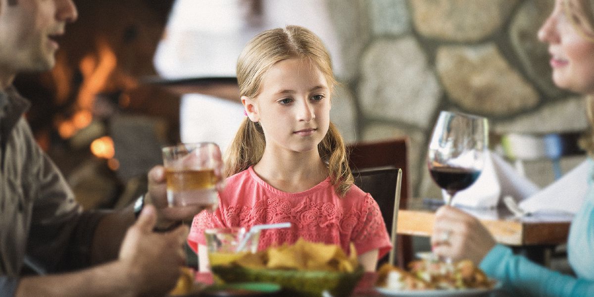 Una niña observa a sus padres tomando bebidas alcohólicas